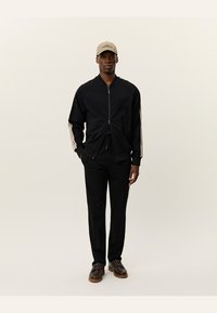 Black zip-up jacket with cream side stripes, paired with black pants. Worn with a beige cap and dark shoes featuring light brown soles.