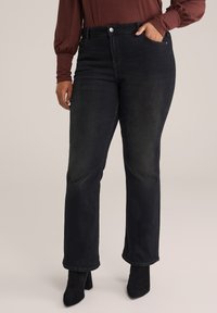 Jeans in denim neri a vita alta con taglio dritto, design a cinque tasche e una leggera scoloritura; abbinati a una maglietta a maniche lunghe e stivali con tacco.