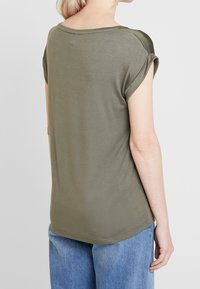 Camicia a maniche corte verde oliva, materiale in cotone morbido, vestibilità rilassata con risvolti e orlo arrotondato, cuciture minime sul colletto.