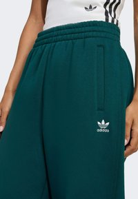 Teal sweatpants med ribbet elastisk talje. Har sidelommer og hvidt Adidas-logo på det nederste ben. Fremstillet af blødt stof.