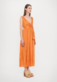Maxiklänning i skrynklig orange tyg, med V-ringning, breda axelremmar, åtsittande midja och en knytning. Matchad med beige plattformssandaler.