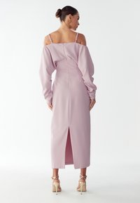 Dlouhé šaty v pastelově růžové barvě s vykrojením na ramínkách, dlouhými rukávy a rozparkem na zadní straně. Hladká textura, přiléhavý korzet a nastavitelné ramínka.