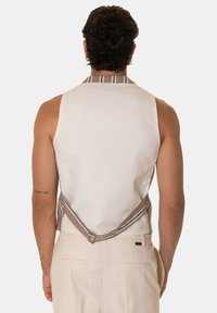 Gilet bianco senza maniche con dettagli a strisce diagonali marroni sul retro, dotato di una chiusura e spalline regolabili.