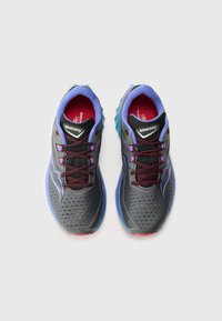 Chaussures de course grises avec des accents bleus et violets, tige perforée, lacets rouges et semelle rembourrée. Marque affichée sur la languette.