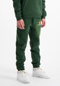 Groene fleece joggers met elastische boorden en een drawstring taille, voorzien van een kleurraf basketball graphic op de linker bovenbeen. Gepaard met witte sneakers.