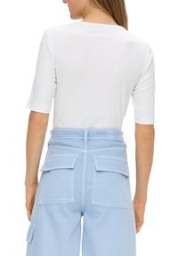 Weißes Kurzarmoberteil kombiniert mit hellblauen Cargo-Hosen, die mehrere Taschen und genähte Details aufweisen und einen lockeren Sitz sowie einen lässigen Stil präsentieren.