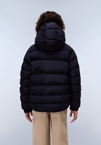 Nafoukaná černá bunda s kapucí, vyrobená z prošívaného materiálu s elastickými manžetami, doplněná béžovými kalhotami s širokými nohavicemi.