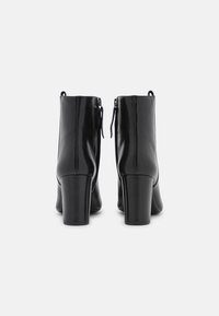 Botines de cuero negro con una textura suave, tacones altos de bloque y cremalleras dobles en la parte trasera para facilitar el uso. Diseño simple y elegante.