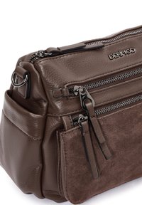 Bolso de cuero marrón y ante con múltiples bolsillos con cremallera, acentos en hardware plateado y un acabado texturizado. Diseño compacto y estructurado.