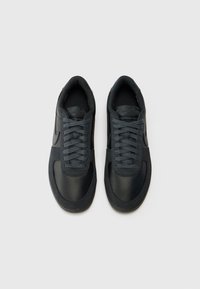 Zapatillas negras con un upper de cuero liso y textil, que cuentan con cordones redondos, un collar acolchado y una suela de goma.