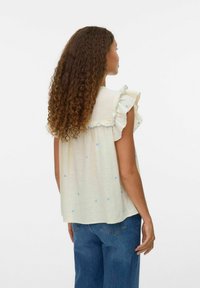 Blusa gialla chiara con maniche a volant, decorata con piccoli cuori blu. Tessuto morbido, vestibilità morbida, indossata con jeans in denim blu.