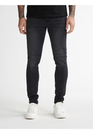 Jean slim noir en denim, avec une texture lisse et un léger délavage. Associé à des baskets blanches pour créer un contraste.