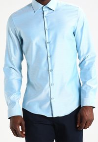 Lichtblauw langemouwen shirt met een subtiele gestreepte textuur, button-down kraag en bijpassende knopen, gecombineerd met donkere broek.