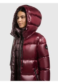 Viininpunainen toppatakki kiiltävällä pinnalla, isolla hupulla ja mustilla metalliosilla. Takissa on vetoketjusuljenta ja sivutaskut.