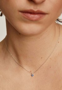 Collar de plata con un pequeño colgante de mariposa con acentos azules, descansando delicadamente sobre la piel desnuda. La cadena es fina y minimalista.