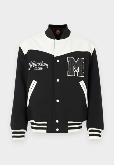 Chaqueta universitaria en blanco y negro con cierre de botones, puños acanalados, dos bolsillos laterales y un gran parche con la letra "M" en el pecho. Bordado "Múnich".