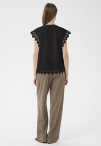 Černý top s obloukovými okraji a krajkovými detaily na ramenou, kombinovaný s hnědými kalhotami s vysokým pasem a proužkem. Hladká textúra látky.