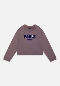 Lilla avkortet sweatshirt med lange ermer. Har marineblå tekst "PARIS" og "TOKYO" trykt i midten. Glatt tekstur, ribbede mansjetter.