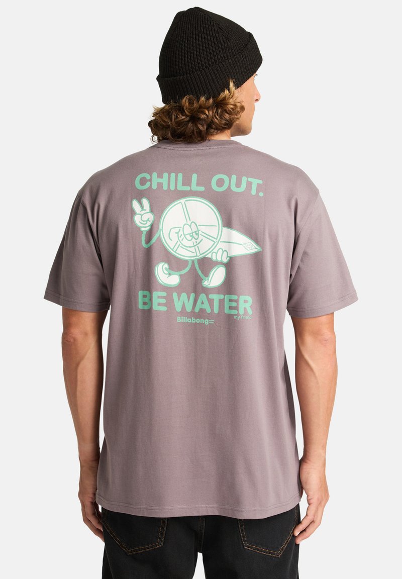 Szürke pamut póló, amelynek hátoldalán egy menta zöld grafikával található a "CHILL OUT. BE WATER" felirat és egy rajzfilmfigura, aki egy szörfdeszkát tart.