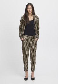 Traje a cuadros negro y beige con blazer ajustado y pantalones ajustados; combinado con una blusa negra y bailarinas negras. Textura de tela suave.
