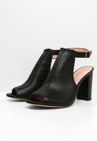 Černé kožené otevřené boty na podpatku se strukturovaným povrchem, kotníkový pásek s zlatou přezkou a designem s blokovým podpatkem.