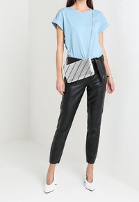 Světlomodré tričko s krátkými rukávy, černé kalhoty z umělé kůže, stříbrná kovová crossbody taška s diagonálními pruhy, bílé lodičky s špičatou špičkou.