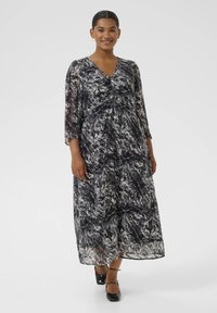 Robe maxi en tissu transparent noir et blanc, avec un décolleté en V, des manches trois-quarts et un motif texturé. Silhouette longue et fluide.