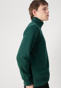 Grønn, høyhalset svettegenser med lange ermer og en tettsittende design. Laget av glatt stoff med ribbede mansjetter og nederkant.