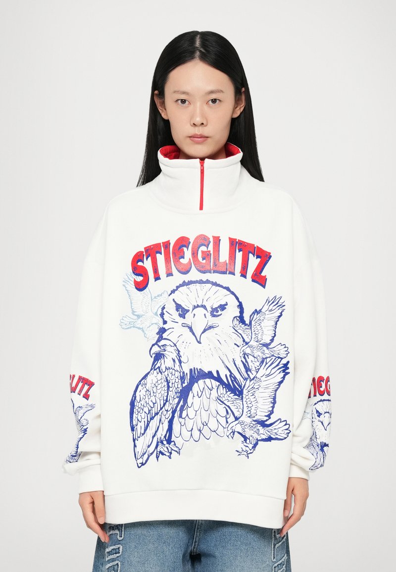 Felpa bianca oversize con colletto alto, caratterizzata da grafiche di uccelli blu e testo rosso "STIEGLITZ" sul petto e sulle maniche.