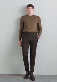 Oliven grønn genser, slim-fit brune bukser og svarte ankelstøvler. Stoffet fremstår som glatt med en tettsittende silhuett.