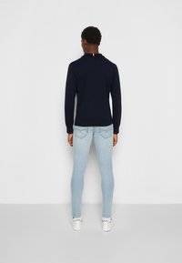 Polo à manches longues bleu marine avec un col orné d'une rayure rouge. Porté avec un jean slim bleu clair et des baskets blanches. Design simple, matériau en coton.