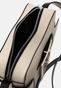 Borsa a mano in pelle beige con dettagli neri, chiusura con zip superiore e una lavorazione testurizzata sul lato. Interno nero. Include una tracolla regolabile.