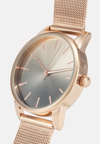 Montre ronde avec un cadran dégradé bleu-vert, index des heures en or rose et bracelet en maille. Le boîtier est en or rose poli avec une couronne.