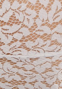 Bílá krajková tkanina s květinovými vzory a jemnými detaily, se vzdušnou strukturou, která poskytuje delikátní a texturovaný vzhled.