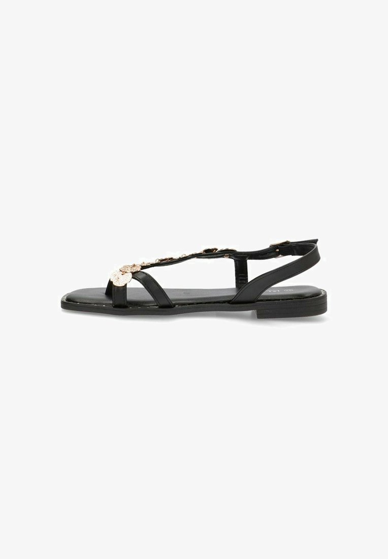 Sandalias de cuero negro con suela plana, con diseño de tira en forma de T y acentos de ferretería decorativa. Textura suave y estilo minimalista.