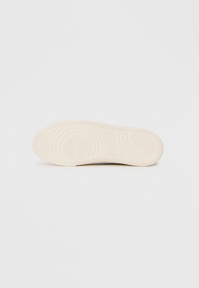 Shoe outsole in off-white rubber, featuring curved tread patterns and a textured surface with branding detail in the center.