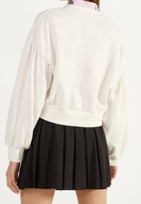 Felpa bianca con maniche a sbuffo, orlo a costine e colletto alto, abbinata a una gonna nera plissettata. Design casual e aderente.