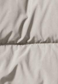 Lichtbeige, gewatteerde stof met een gladde textuur, met zachte plooien en een gestikte naad die horizontaal door het midden loopt.