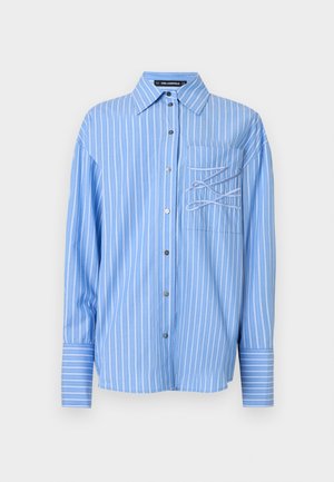 Svetlo modra srajca z navpičnimi črtami, z žepom na prsih in edinstvenim zankastim detajlom na žepu. Dolgi rokavi.