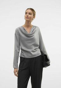 Maglione grigio con collo a cowl e maniche lunghe, realizzato in tessuto morbido, abbinato a pantaloni neri con righe sottili, caratterizzati da un design elegante e una vestibilità raffinata.