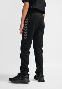 Schwarze Jogginghosen mit texturierter Oberfläche, ausgestattet mit einem kontrastierenden grauen Chevron-Muster an den Seiten und einem elastischen Bund.