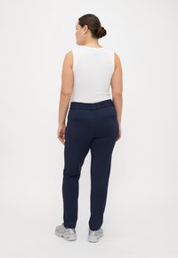 Marineblaue Hose mit einem strukturierten elastischen Bund, ausgestattet mit zwei Gesäßtaschen, kombiniert mit einem weißen ärmellosen Oberteil und silbernen Turnschuhen.