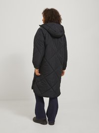 Manteau long rembourré noir à capuche avec un motif matelassé en losanges, avec une texture lisse et des fentes latérales, associé à un jean large sombre.