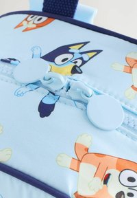 Kék szövet hátizsák játékos rajzfilm állatmintákkal, cipzáras záródással, lekerekített húzófülekkel és megerősített felső fogantyúval a hordozáshoz.