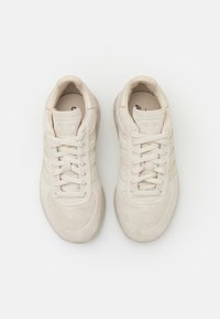 Ζευγάρι μπεζ σουέτ αθλητικών παπουτσιών Adidas με κορδόνια, εμφανίζοντας την άνω πλευρά σε λευκό φόντο.