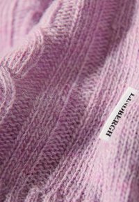 Gestrickter Pullover in Helllila, mit strukturierten Mustern und einem weichen, flauschigen Aussehen. Beinhaltet ein kleines Stoffetikett am Rand.