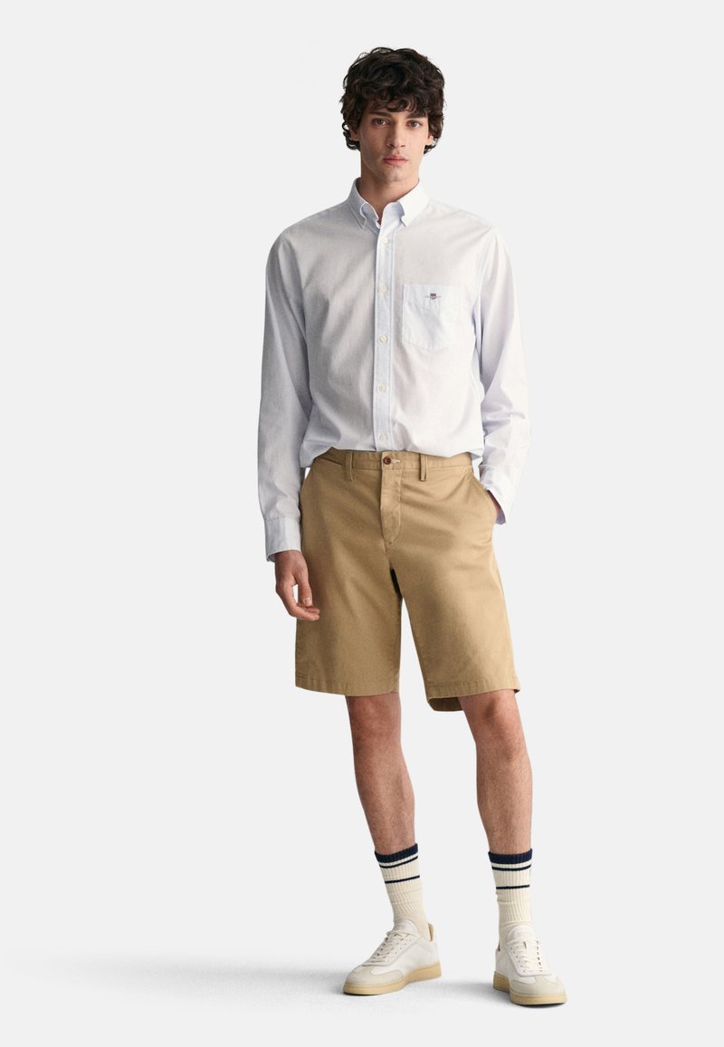 Herreoutfit bestående av en lys blå skjorte med knapper, khaki shorts, hvite sneakers og kremfargede sokker med marineblå striper.