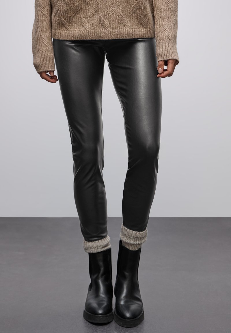 Černé legíny z umělé kůže se slim fit, doplněné pletenými návleky na boty v světle šedé barvě, nošeny s černými kotníkovými botami.