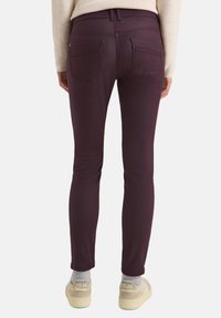 Mørke burgunder skinny jeans lavet af strækbart stof. Funktioner inkluderer to baglommer og en mellemhøj talje. Stylet med lyse fodtøj.