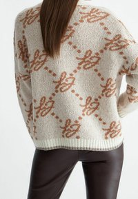 Suéter de punto con base crema y patrón de lazo en color óxido. Cuenta con dobladillo y puños acanalados, ajuste holgado y textura suave.